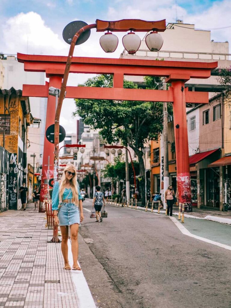 Me walking in front of a red Torii gate in the Liberdade district, one of the best places to visit in Sao Paulo.