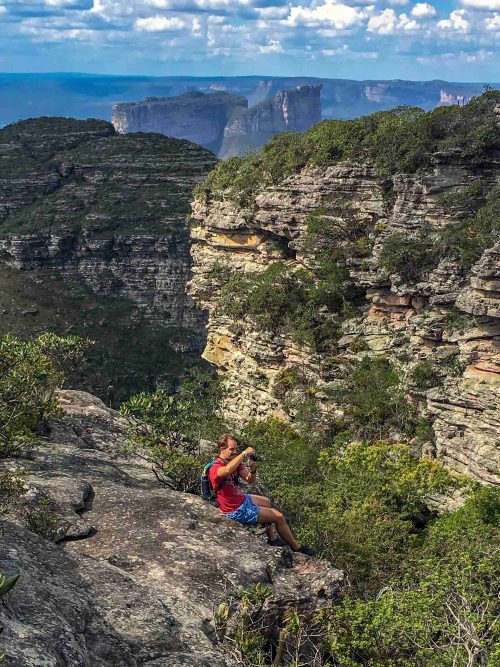 A man sitting on a rock and photographing the scenery while being surrounded by otherworldly cliffs