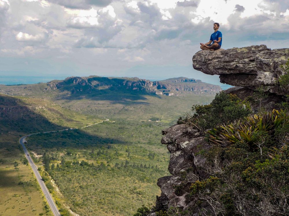 a man sitting on the edge of a cliff and meditating with a view of the valleys and mountains of Chapada Diamantina around him