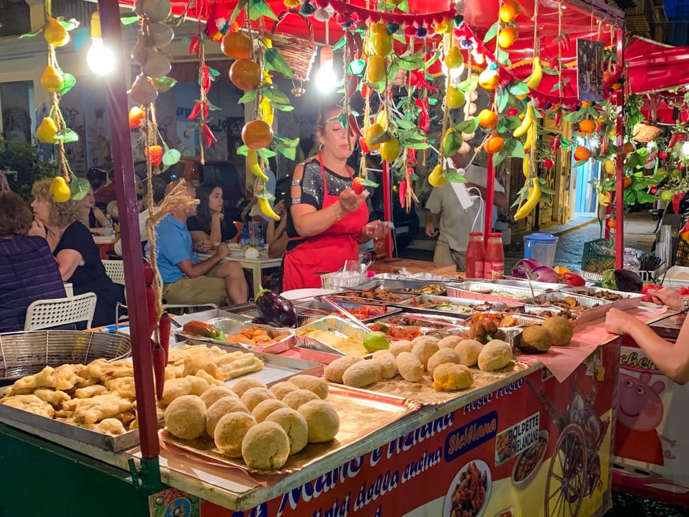 A market stand decorated with plastic fruit, displaying various types of street food in Palermo.