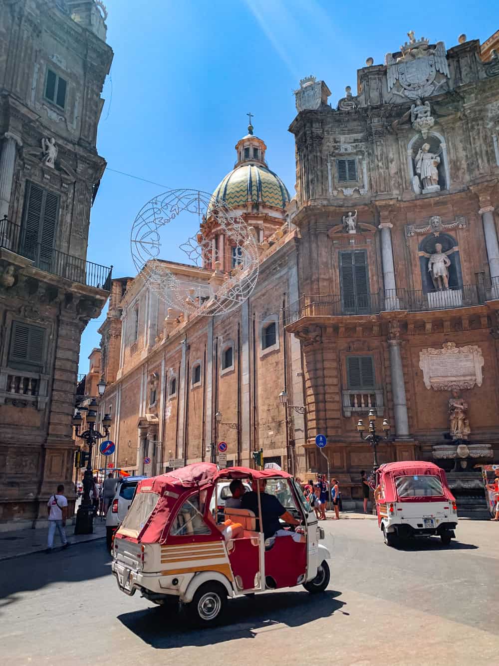 Red tuk-tuks driving across Quattro Canti square in the historic center of Palermo.