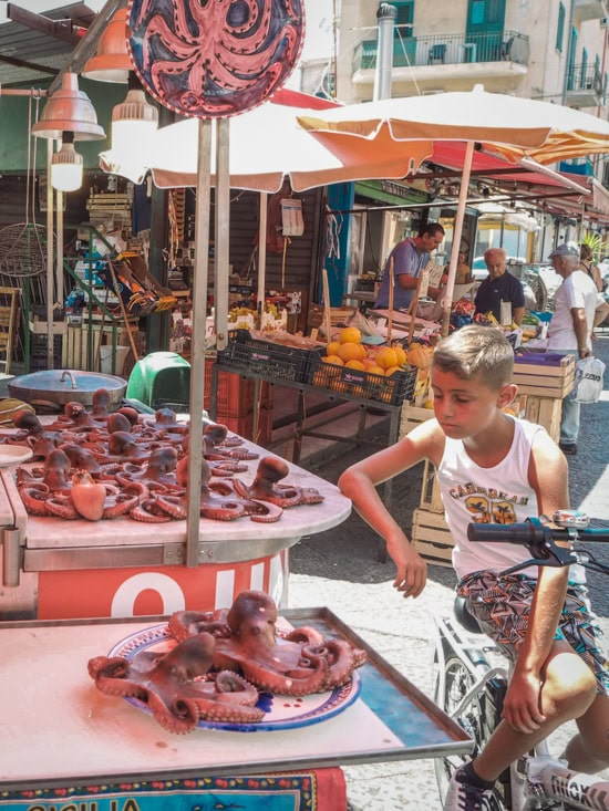 A boy on a bicycle looking at octopuses sold at a street market in Palermo.
