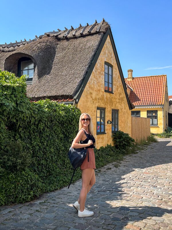 Me standing on a cobblestone street in Dragør, next to a traditional house with a thatched roof and yellow-painted walls.