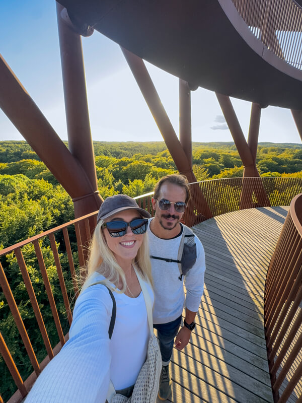 A selfie of my husband and I standing on the ramp of The Forest Tower with a view over a forest in the background.