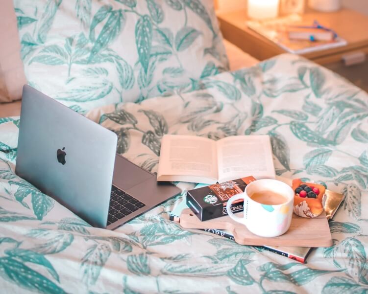 A laptop and a cup of coffee in bed - the perfect cozy setting to watch sustainable travel documentaries during COVID-19 self-isolation