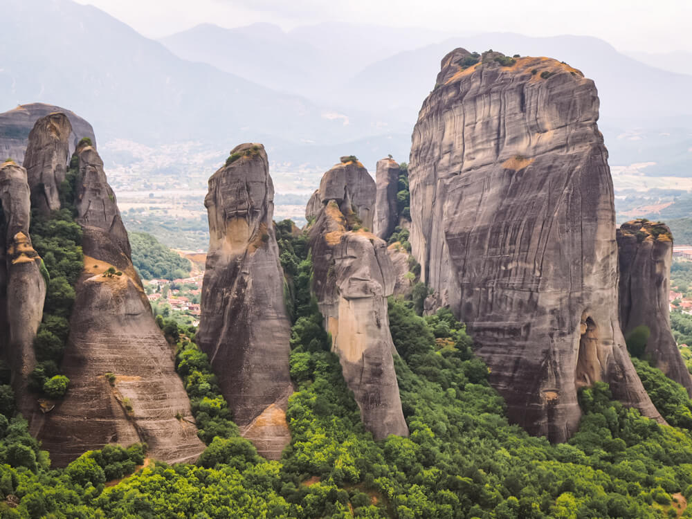 A series of tall narrow sandstone mountains with lush green forest at their base in Meteora, Greece.