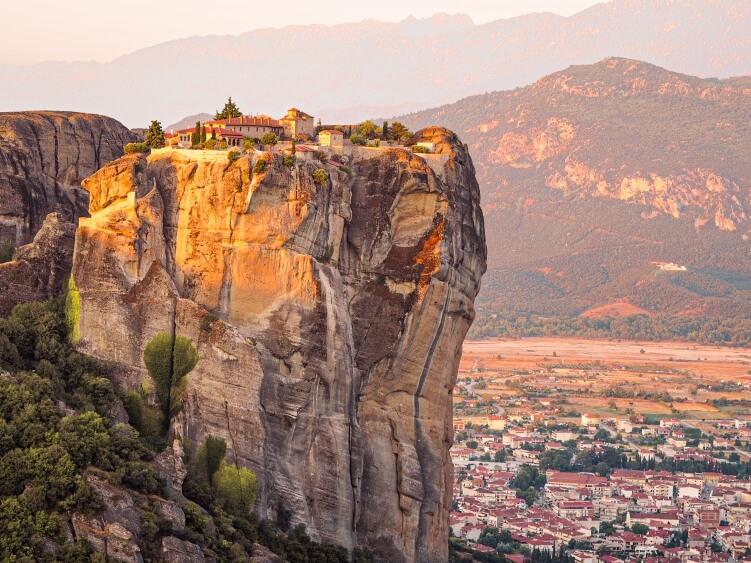 View over The Holy Trinity Monastery perched on top of a steep vertical boulder during sunrise in Meteora near the town of Kalambaka