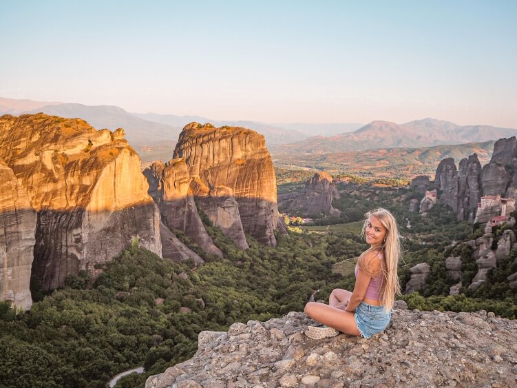 Me sitting on a rock surrounded by spectacular rocky scenery and green valleys of Meteora during sunrise