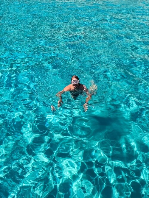 a man with a snorkeling mask swimming in the clear neon blue waters of Gerakas Beach, one of the best things to do in Milos, Greece