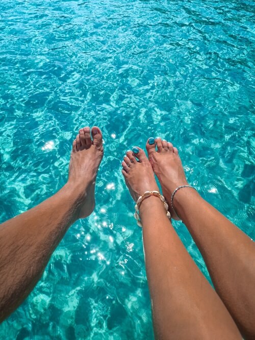 Bare feet hanging over the edge of the boat above the vibrant turquoise sea at Gerakas Beach