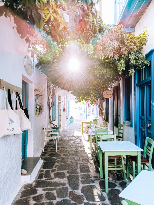 A narrow cobblestone alleyway between whitewashed houses with blue doors and windows at Plaka.