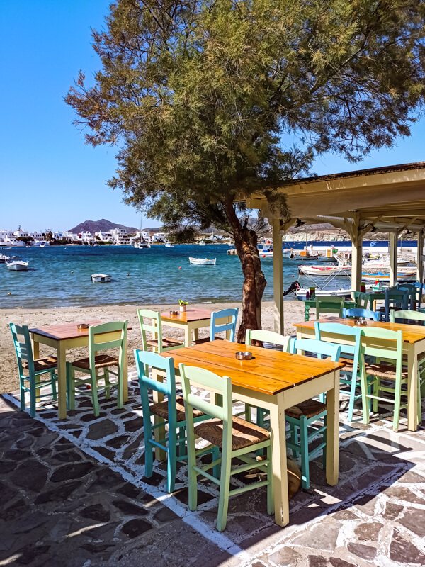 Wooden tables and pastel-colored chairs at a beachfront restaurant overlooking the sea in the village of Pollonia.