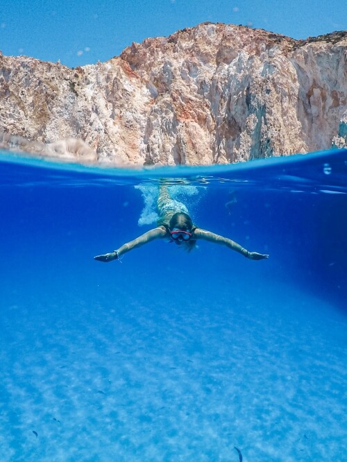 me swimming underwater in the azure sea around Polyaigos island with tall white cliffs behind me