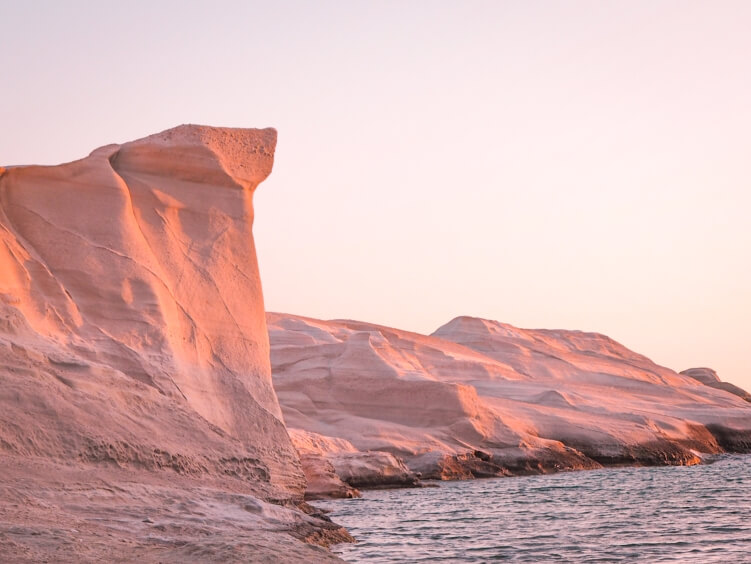 White volcanic cliffs of Sarakiniko Beach illuminated by warm pink light during sunrise