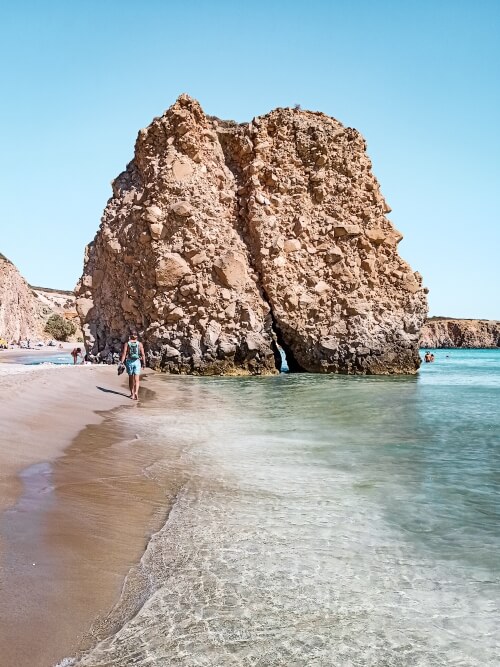 A large beige rock jutting out of the crystal clear water on Firiplaka Beach