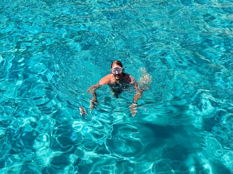 A man with a snorkeling mask swimming in the clear turquoise waters of Gerakas Beach, one of the best Milos beaches