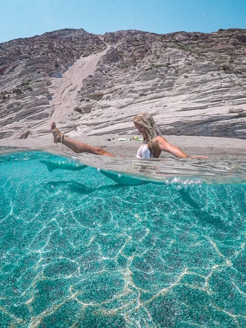 Me sitting in the shallow neon blue water of Gerakas Beach, with white rocky shore in the background