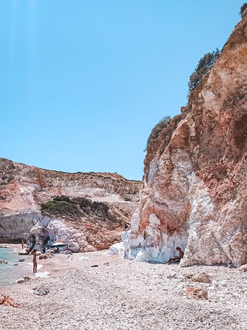 A narrow stretch of white pebbles next to a vertical rock wall at Kastanas Beach in a remote part of Milos