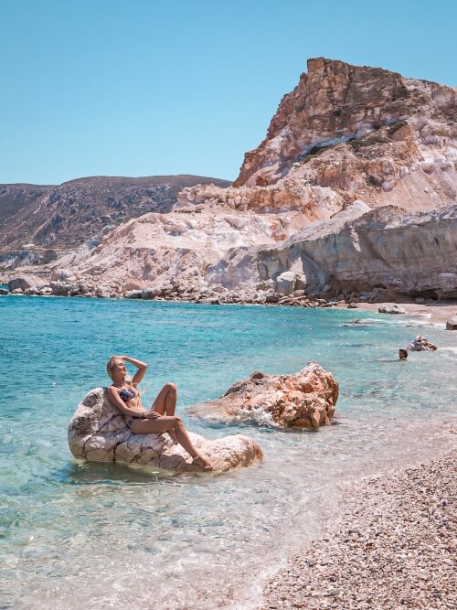 Me sunbathing on a rock in the clear blue waters of Kastanas Beach with a rugged orange mountain behind me