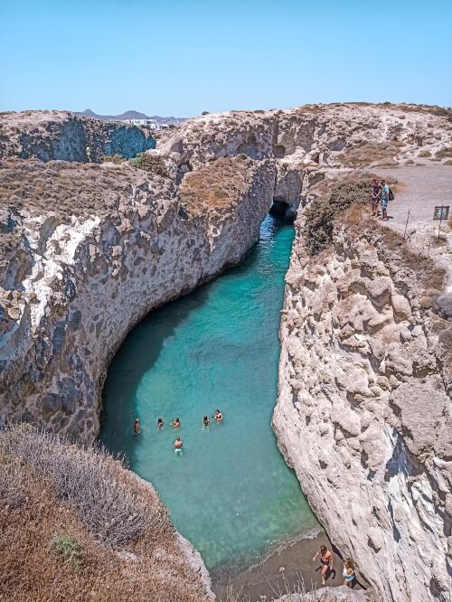 A narrow inlet of turquoise water surrounded by vertical rock walls at Papafragas Beach in Milos, Greece