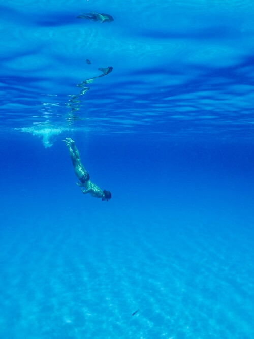 An underwater shot of a man diving down into the clear blue water at Polyaigos 