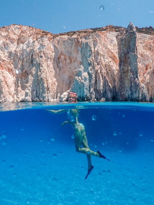 Me floating in the sapphire blue water, wearing fins and a snorkeling mask, with the pastel colored cliffs of Polyaigos behind me