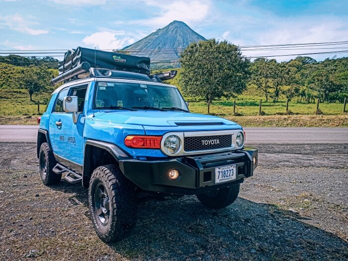 Blue 4x4 car with a rooftop in front of Arenal Volcano