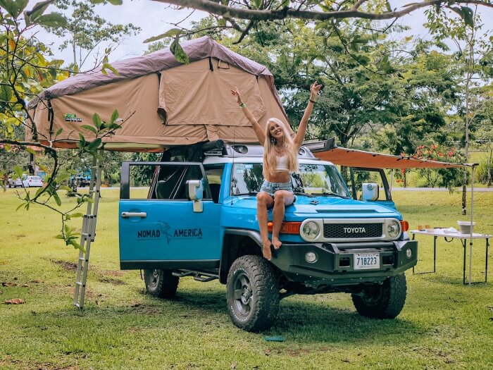A girl sitting on a blue 4x4 car with a beige rooftop tent, the perfect setup for a Costa Rica road trip