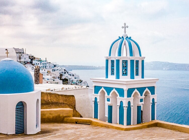 White and blue church dome with a backdrop of Aegean sea, a view on the hike from Fira to Oia in Santorini