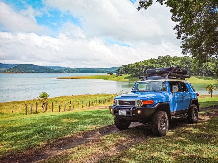 Blue 4x4 car driving on a dirt road next to Lake Arenal