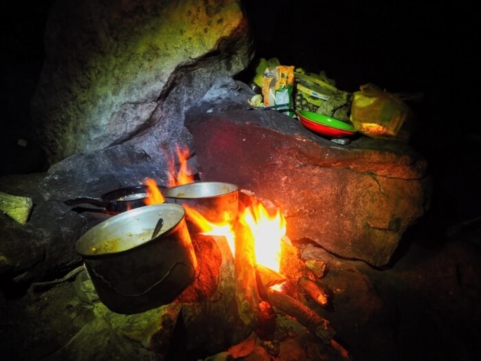 Pots and pans on top of a bonfire in a campsite kitchen at night