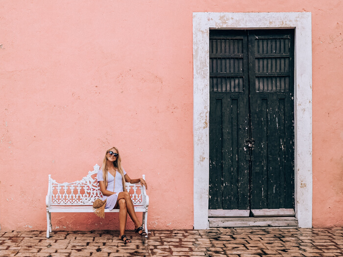 A girl sitting on a white bench in front of a pink wall in Valladolid, Mexico's colorful colonial town