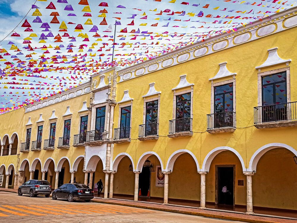 A yellow colonial building decorated with colorful flags in Valladolid, Mexico