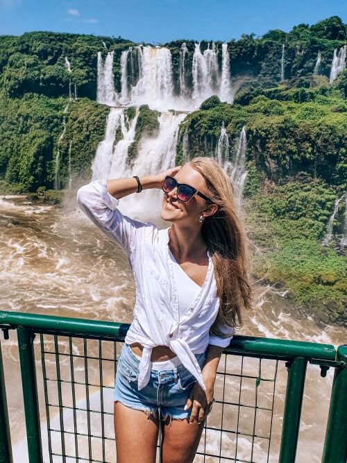 a woman posing on a walkway in front of the cascades of Iguassu Falls