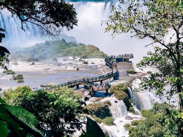 Visitors standing on an elevated footbridge above a river with a view of Devil's Throat at Iguacu Falls