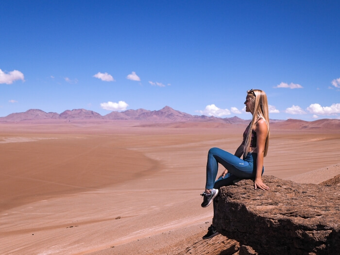 A woman sitting on a rock and admiring the view over the Atacama Desert on Ruta de Los Salares