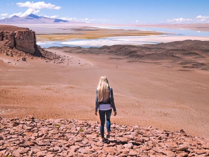 A woman standing on a rocky hill overlooking Salar de Tara salt flat, one of the most amazing places to visit in Atacama Desert