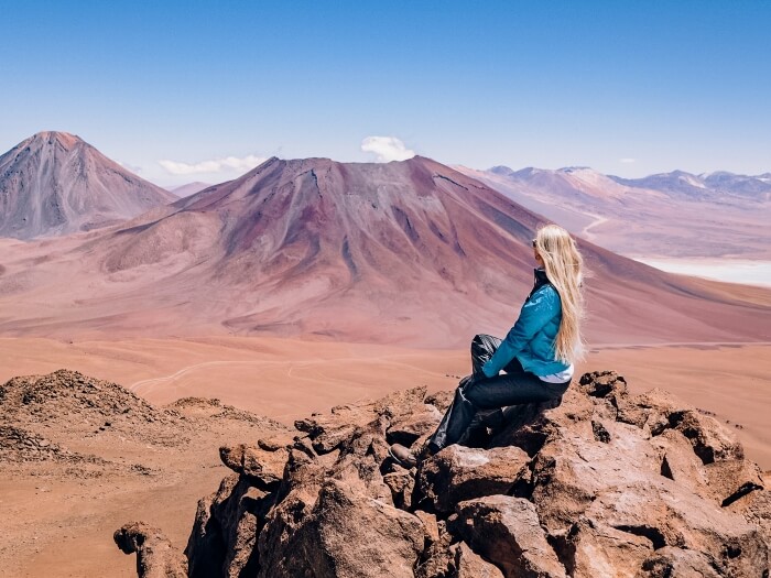Me sitting on a rock, admiring a panoramic view from the summit of Cerro Toco volcano, one of the best Atacama Desert trekking tours