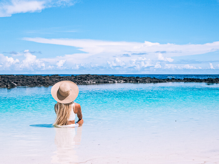 A woman sitting in a shallow lagoon full of crystal clear water at Tortuga Bay on Galapagos Islands