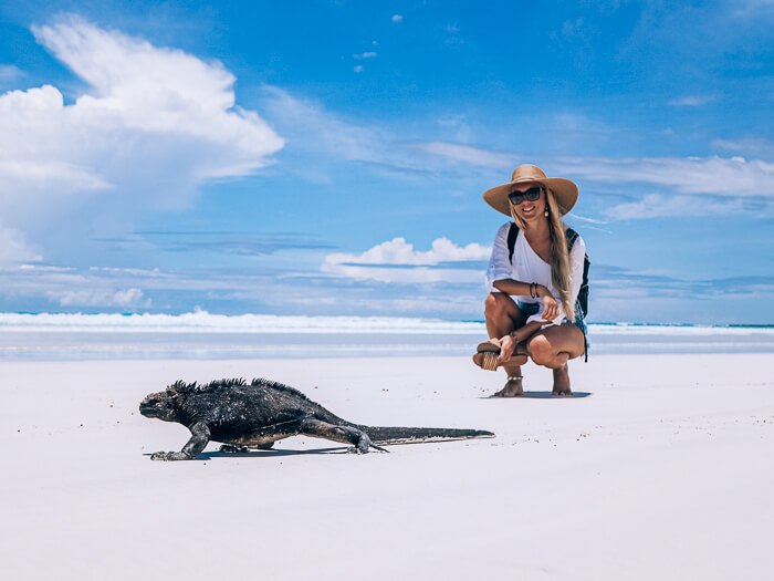 Me squatting next to a black marine iguana on the white sand at Tortuga Bay, one of the best places to visit in Galapagos