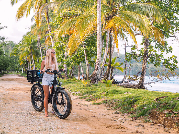 A girl biking on a palm tree-lined coastal dirt road on Isla Colon, Panama