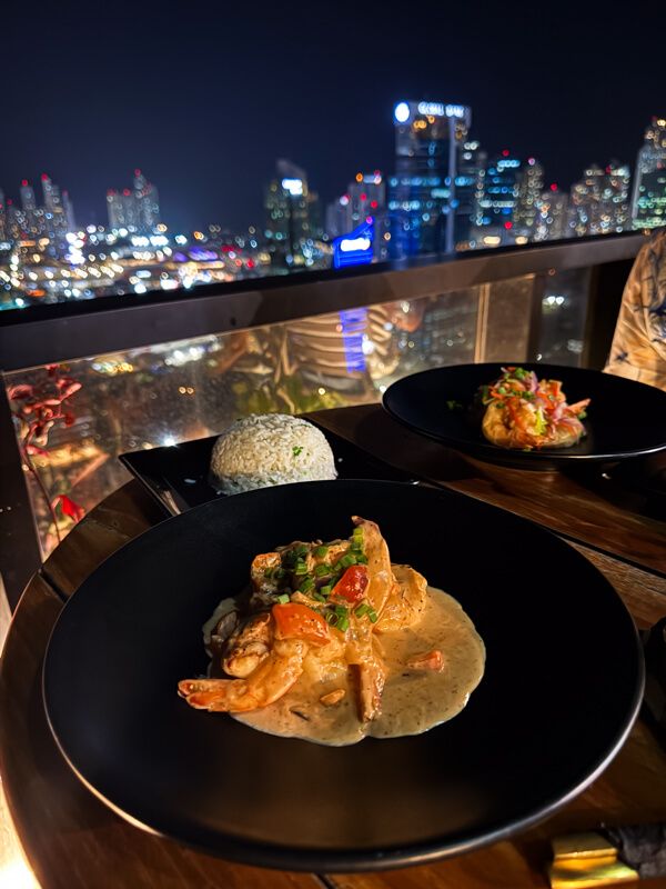 A plate of coconut curry with a view of high-rise buildings in the background at night.