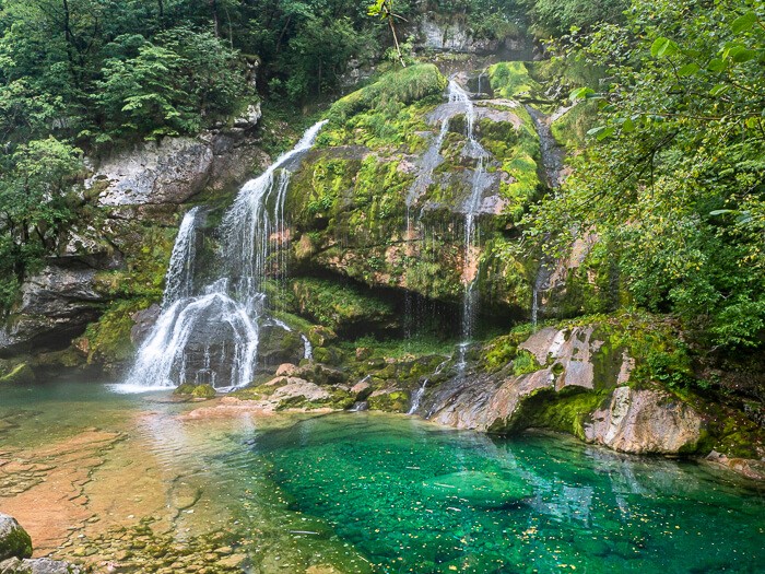 An emerald pool and lush vegetation surrounding the small but beautiful Slap Virje Waterfall near the town of Bovec