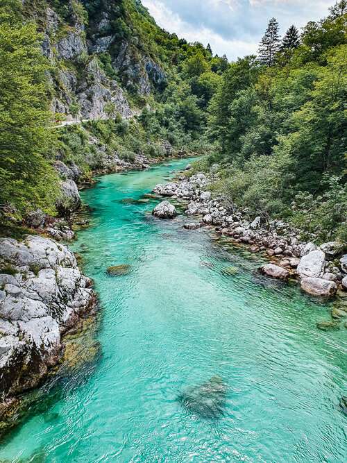 Bright blue Soca River and its rocky shores surrounded by a forest.