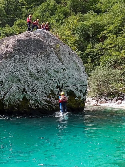 tourists jumping from a cliff into an emerald river