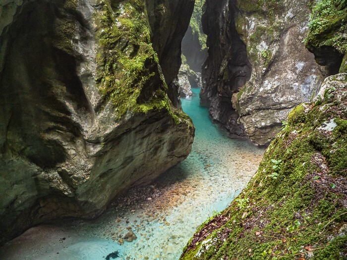 Shallow bright blue river nestled between vertical rock walls covered with moss at Tolmin Gorge.