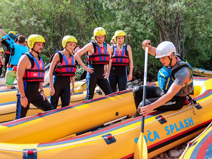 A group of people standing next to a yellow raft and observing the rafting instructor