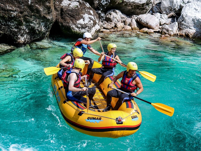 A group of people sitting in an inflatable raft, wearing life jackets and helmets on the Soca River, the best river for rafting in Slovenia