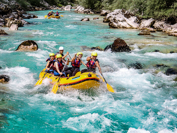 People sitting in a raft and paddling through the frothy rapids of Soca River, the best place for white water rafting in Slovenia