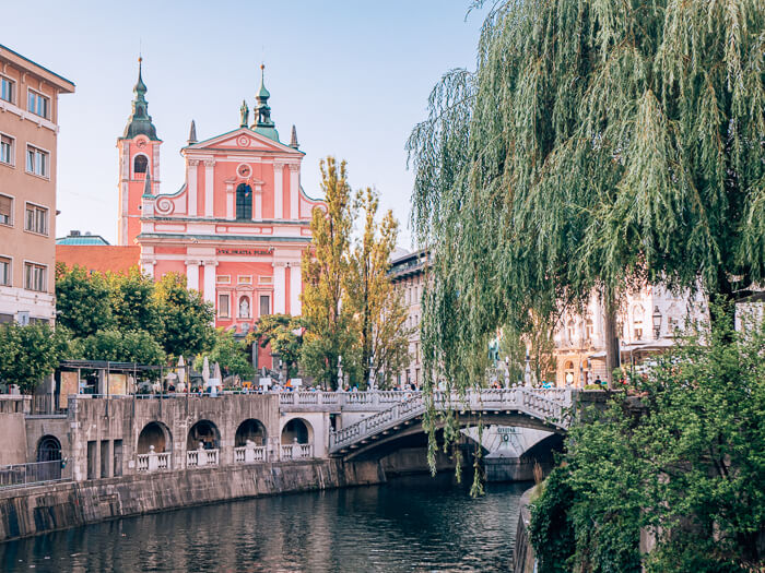 Triple Bridge and the pink Franciscan Church next to a river in Ljubljana old town